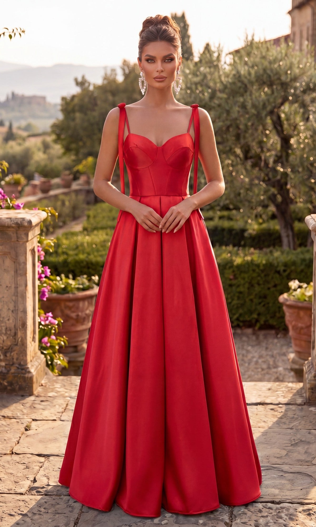 Wearing the Long Prom Dress: Chicas DM8033 in red, a woman with spaghetti straps and a subtle sweetheart neckline stands outdoors on a stone path, surrounded by greenery and stone planters.